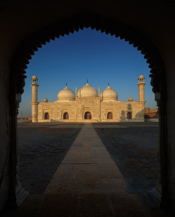 View of the historic white marble Abbasi Mosque with its prominent domes and minarets framed by an arched entrance in Derawar Punjab Pakistan.