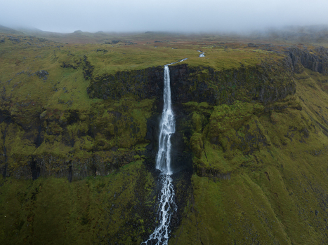 Aerial view of a slender waterfall cascading down a verdant cliff face under a misty sky Snæfellsnes Eyja og Miklaholtshreppur Iceland. Aerial view of a slender waterfall cascading down a verdant cliff face under a misty sky Snæfellsnes Eyja og Miklaholtshreppur Iceland.