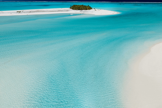 Aerial view of the small island of Aitutaki surrounded by vibrant turquoise lagoon waters and white sandbanks in the Cook Islands. Aerial view of the small island of Aitutaki surrounded by vibrant turquoise lagoon waters and white sandbanks in the Cook Islands.