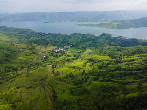 Aerial view of the lush green landscape of Kaas plateau with rolling hills a small village and a large reservoir in Satara Maharashtra India.