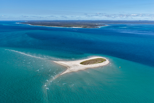 Aerial view of Pelican Bank a small sand island surrounded by turquoise and deep blue ocean waters with the larger K gari island visible in the distance in K gari Queensland Australia. Aerial view of Pelican Bank a small sand island surrounded by turquoise and deep blue ocean waters with the larger K gari island visible in the distance in K gari Queensland Australia.