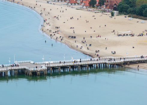 Aerial view of Sopot Pier extending into the Baltic Sea with people walking along the wooden structure and a sandy beach with visitors in Sopot Pomeranian Voivodeship Poland. Aerial view of Sopot Pier extending into the Baltic Sea with people walking along the wooden structure and a sandy beach with visitors in Sopot Pomeranian Voivodeship Poland.