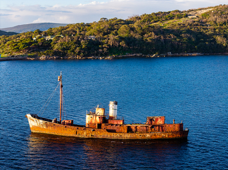 Aerial view of a rusty shipwreck floating in the deep blue water near the forested coastline of the Vancouver Peninsula Western Australia Australia. Aerial view of a rusty shipwreck floating in the deep blue water near the forested coastline of the Vancouver Peninsula Western Australia Australia.