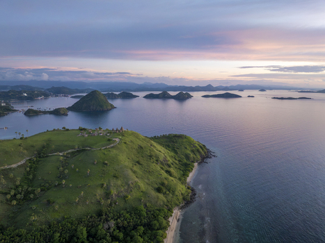 Aerial view of the lush green hills of Labuan Bajo with traditional structures overlooking the calm sea and distant islands under a soft sunset sky in Komodo East Nusa Tenggara Indonesia. Aerial view of the lush green hills of Labuan Bajo with traditional structures overlooking the calm sea and distant islands under a soft sunset sky in Komodo East Nusa Tenggara Indonesia.