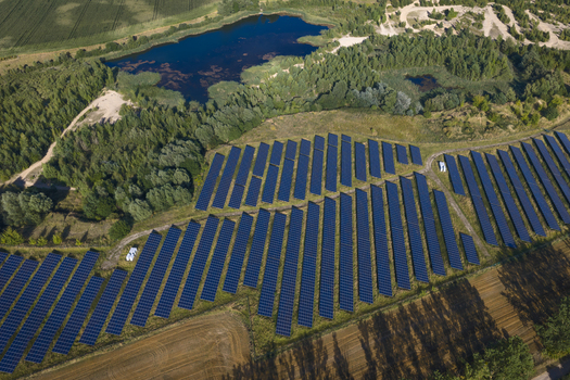 Aerial view of a large solar farm with rows of photovoltaic panels situated next to a small lake and surrounded by green forests and agricultural fields in Uckermark Brandenburg Germany. Aerial view of a large solar farm with rows of photovoltaic panels situated next to a small lake and surrounded by green forests and agricultural fields in Uckermark Brandenburg Germany.