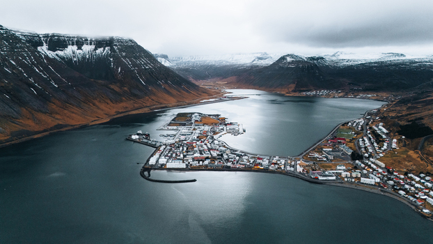 Aerial view of a quaint town nestled between dark mountains capped with snow and the still reflective waters of the fjord Ísafjörður Iceland. Aerial view of a quaint town nestled between dark mountains capped with snow and the still reflective waters of the fjord Ísafjörður Iceland.