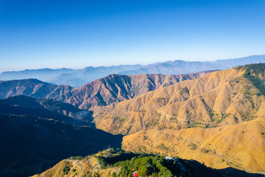 Aerial view of the rolling Himalayan foothills with winding mountain roads and lush ridges under a clear blue sky in Chakrata Uttarakhand India. Aerial view of the rolling Himalayan foothills with winding mountain roads and lush ridges under a clear blue sky in Chakrata Uttarakhand India.