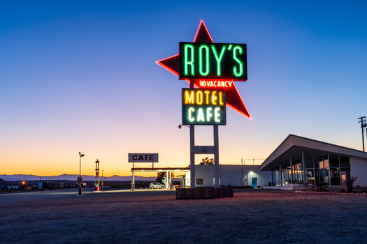 Amboy United States 07 April 2026 View of Roy s Motel and Cafe neon sign glowing warmly against the cool desert twilight casting long shadows across the empty ground. Amboy United States 07 April 2026 View of Roy s Motel and Cafe neon sign glowing warmly against the cool desert twilight casting long shadows across the empty ground.