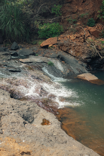 View of water cascading over rocks into a serene pool framed by rugged cliffs and verdant vegetation a natural oasis Chiplun Maharashtra India.