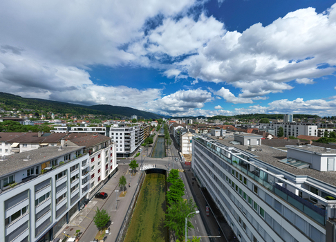 Aerial view of modern apartment buildings along a straight canal under a cloudy blue sky with mountains in the distance Biel Bienne Canton of Bern Switzerland. Aerial view of modern apartment buildings along a straight canal under a cloudy blue sky with mountains in the distance Biel Bienne Canton of Bern Switzerland.