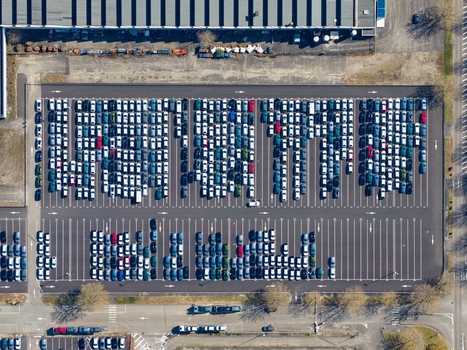 Aerial view of neatly arranged rows of cars in a vast parking lot reflecting the sunlight contrasting with the surrounding industrial buildings Sausheim Grand Est France.