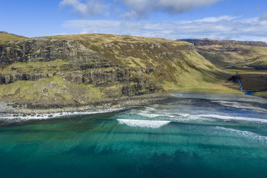 Aerial view of Talisker Bay Beach with turquoise waves crashing against the dark cliffs and rugged hills Isle of Skye Scotland United Kingdom. Aerial view of Talisker Bay Beach with turquoise waves crashing against the dark cliffs and rugged hills Isle of Skye Scotland United Kingdom.