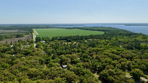 Aerial view of Sixmile Creek winding through lush green forests and expansive agricultural fields under a clear blue sky in St. Johns County Florida United States.