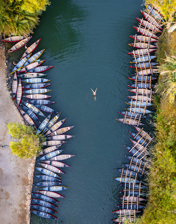 Aerial view of a swimmer embraced by the cool dark waters framed by parallel rows of canoes and the lush greenery of Kineret Israel.