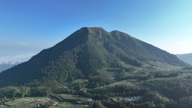 Aerial view of a lush green mountain with terraced fields and dense forest under a clear blue sky in Kecamatan Ngablak Jawa Tengah Indonesia. Aerial view of a lush green mountain with terraced fields and dense forest under a clear blue sky in Kecamatan Ngablak Jawa Tengah Indonesia.