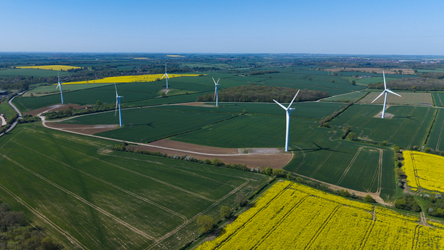 Aerial view of the New Albion Wind Farm with white turbines standing in vibrant green and yellow rapeseed fields under a clear blue sky in Rushton England United Kingdom. Aerial view of the New Albion Wind Farm with white turbines standing in vibrant green and yellow rapeseed fields under a clear blue sky in Rushton England United Kingdom.