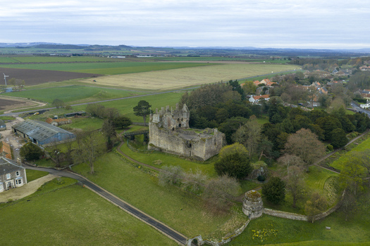 Aerial view of Dirleton Castle and Gardens featuring historic stone ruins lush green lawns and surrounding trees in Dirleton Scotland United Kingdom. Aerial view of Dirleton Castle and Gardens featuring historic stone ruins lush green lawns and surrounding trees in Dirleton Scotland United Kingdom.