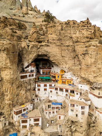 Aerial view of Phukthal Gompa a historic Buddhist monastery built into a cliffside cave with white and yellow buildings surrounded by rugged mountain terrain in Phukthal Ladakh India.
