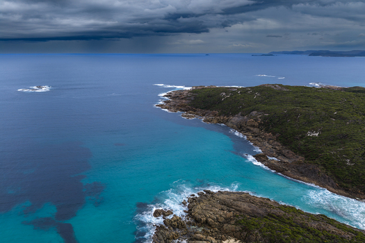 Aerial view of Conspicuous Cliff with turquoise waters crashing against the rocky coastline under dark storm clouds in Nornalup Western Australia Australia. Aerial view of Conspicuous Cliff with turquoise waters crashing against the rocky coastline under dark storm clouds in Nornalup Western Australia Australia.