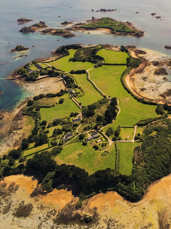Aerial view of lush green landscapes stone walls and scattered houses on the island of Ile de Brehat surrounded by rocky coastline and blue waters in Ile de Brehat Brittany France.