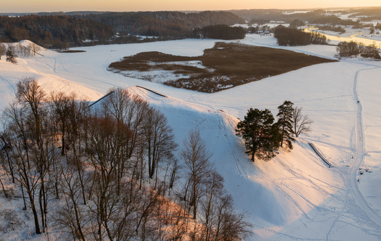 Aerial view of the Kernave Archaeological Site with snow covered hillforts bare trees and frozen fields under golden sunset light Kernave Vilnius County Lithuania.
