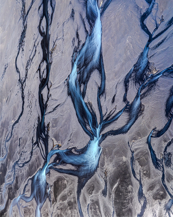 Aerial view of intricate blue glacial meltwater channels flowing through dark volcanic sand deposits in Iceland. Aerial view of intricate blue glacial meltwater channels flowing through dark volcanic sand deposits in Iceland.