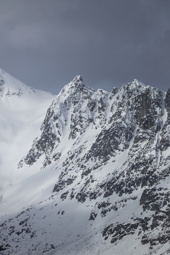 View of jagged snow covered mountain peaks under a dramatic overcast sky in the arctic wilderness Ersfjord Troms Norway. View of jagged snow covered mountain peaks under a dramatic overcast sky in the arctic wilderness Ersfjord Troms Norway.