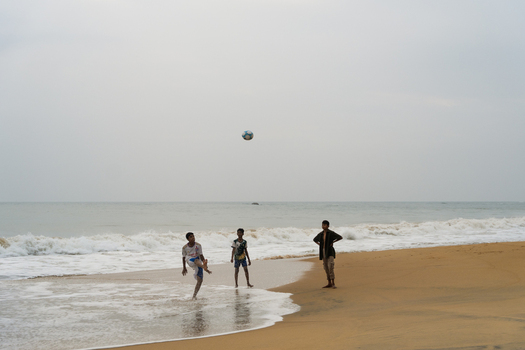 Sri Lanka 30 January 2026 View of three boys playing football on a sandy beach with ocean waves and an overcast sky.
