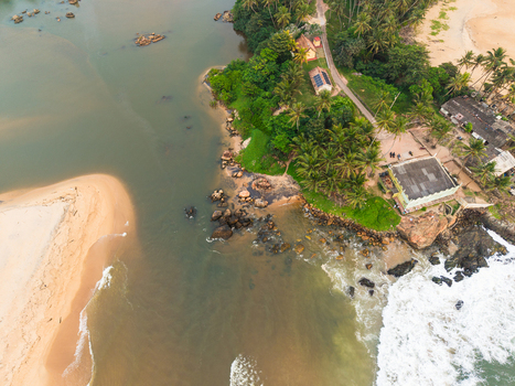 Aerial view of a tropical coastline where a river meets the ocean featuring sandy beaches lush palm trees and small coastal buildings in Galle Southern Province Sri Lanka.