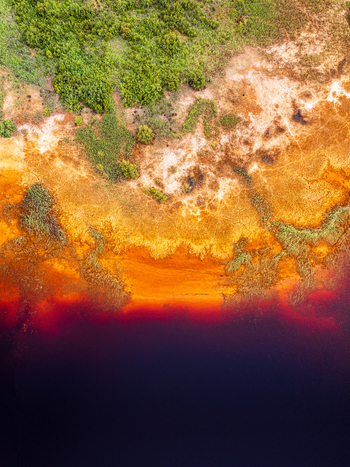 Aerial view of the vibrant red and orange riverbank contrasting with lush green vegetation and dark water in Andalusia Spain. Aerial view of the vibrant red and orange riverbank contrasting with lush green vegetation and dark water in Andalusia Spain.