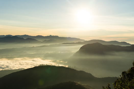 View of Adam s Peak surrounded by misty mountain ridges and a bright morning sun in Ratnapura Sabaragamuwa Province Sri Lanka. View of Adam s Peak surrounded by misty mountain ridges and a bright morning sun in Ratnapura Sabaragamuwa Province Sri Lanka.