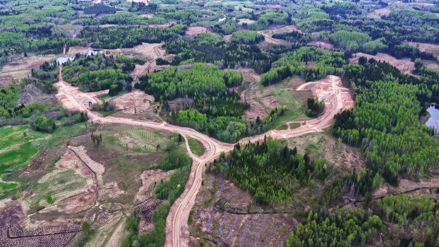 Aerial view of a dirt access road winding through a rural landscape with forests and fields in Latvija. Aerial view of a dirt access road winding through a rural landscape with forests and fields in Latvija.