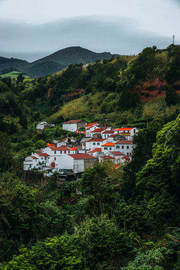 View of white houses with red roofs nestled among vibrant green trees and hills under an overcast sky Furnas Azores Portugal.