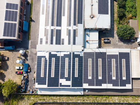 Aerial view of an industrial facility featuring extensive rooftop solar panel arrays surrounding parking areas and green space in Melegnano Lombardy Italy.