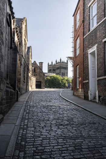 View of the historic cobblestone street leading towards the iconic Durham Cathedral framed by traditional brick and stone buildings in Durham England United Kingdom. View of the historic cobblestone street leading towards the iconic Durham Cathedral framed by traditional brick and stone buildings in Durham England United Kingdom.