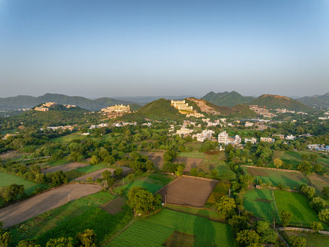 Aerial view of the lush green landscape and agricultural fields surrounding the hills and buildings in the outskirts of Udaipur Rajasthan India.