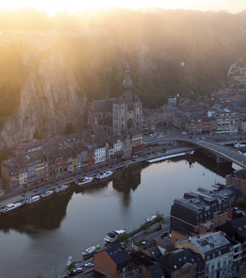 Aerial view of the Collegiate Church of Notre Dame de Dinant nestled against a dramatic limestone cliff along the Meuse River at golden hour in Dinant Wallonia Belgium. Aerial view of the Collegiate Church of Notre Dame de Dinant nestled against a dramatic limestone cliff along the Meuse River at golden hour in Dinant Wallonia Belgium.