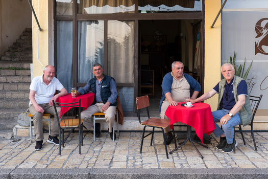 Kruje Albania 12 June 2026 View of four men sitting at small tables with red tablecloths outside a local cafe on a stone paved street.