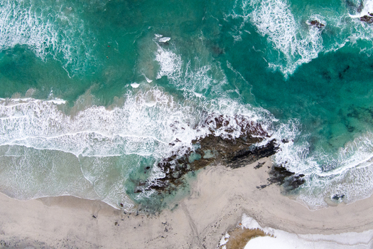 Aerial view of the turquoise waters and white sandy beach of Lofoten with dark rocky formations and crashing waves along the coastline Nordland Norway.