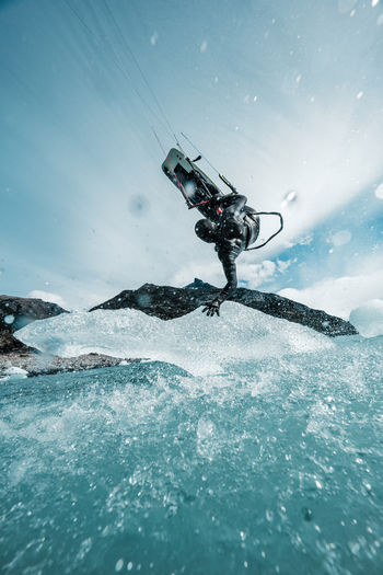 View of a kitesurfer in a wetsuit performing a jump over icy water near the Perito Moreno glacier with mountains in the background in Perito Moreno Santa Cruz Province Argentina. View of a kitesurfer in a wetsuit performing a jump over icy water near the Perito Moreno glacier with mountains in the background in Perito Moreno Santa Cruz Province Argentina.