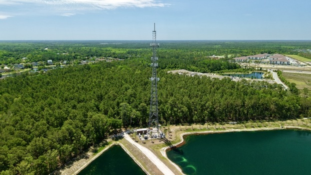 Aerial view of a tall telecommunications tower standing amidst a dense green forest next to a blue pond in World Golf Village Florida United States. Aerial view of a tall telecommunications tower standing amidst a dense green forest next to a blue pond in World Golf Village Florida United States.
