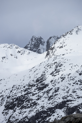 View of snow covered mountain peaks and rocky slopes under an overcast winter sky in Ersfjord Troms Norway. View of snow covered mountain peaks and rocky slopes under an overcast winter sky in Ersfjord Troms Norway.