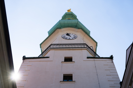 View of the historic Michael s Gate tower featuring its white facade clock face and green copper spire under a clear sky in Bratislava Bratislava Region Slovakia. View of the historic Michael s Gate tower featuring its white facade clock face and green copper spire under a clear sky in Bratislava Bratislava Region Slovakia.