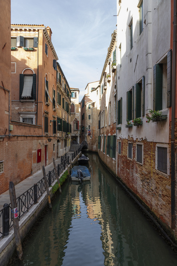 View of a narrow canal lined with historic buildings and shuttered windows featuring small boats moored in the water in Venice Veneto Italy. View of a narrow canal lined with historic buildings and shuttered windows featuring small boats moored in the water in Venice Veneto Italy.