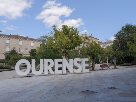 View of the large Ourense city sign in a public square surrounded by trees and historic stone buildings in Ourense Province of Ourense Spain.