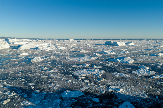 Aerial view of Ilulissat glacier with numerous icebergs floating in the dark arctic sea under a clear blue sky in Greenland. Aerial view of Ilulissat glacier with numerous icebergs floating in the dark arctic sea under a clear blue sky in Greenland.