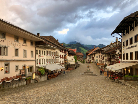 Gruyeres Switzerland 14 May 2026 View of the cobblestone main street of the medieval village with traditional hotels a fountain and people walking under a cloudy sky. Gruyeres Switzerland 14 May 2026 View of the cobblestone main street of the medieval village with traditional hotels a fountain and people walking under a cloudy sky.