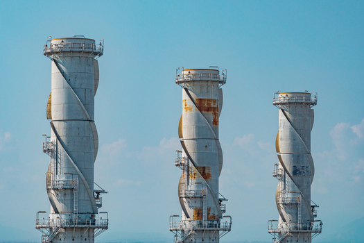 Aerial view of three distinctive exhaust stacks rising above a modern combined cycle power plant under a clear blue sky in Chivasso Piedmont Italy. Aerial view of three distinctive exhaust stacks rising above a modern combined cycle power plant under a clear blue sky in Chivasso Piedmont Italy.