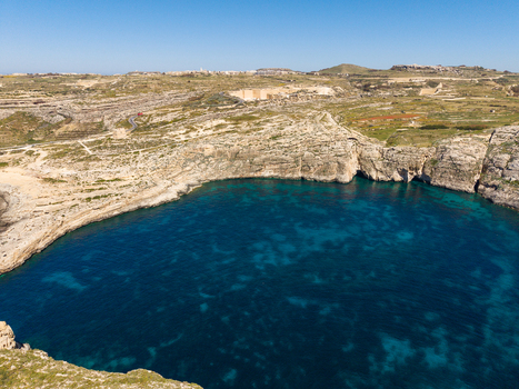 Aerial view of Dwejra Bay with its deep blue waters surrounded by rugged limestone cliffs and arid landscape in Gozo Region Malta. Aerial view of Dwejra Bay with its deep blue waters surrounded by rugged limestone cliffs and arid landscape in Gozo Region Malta.