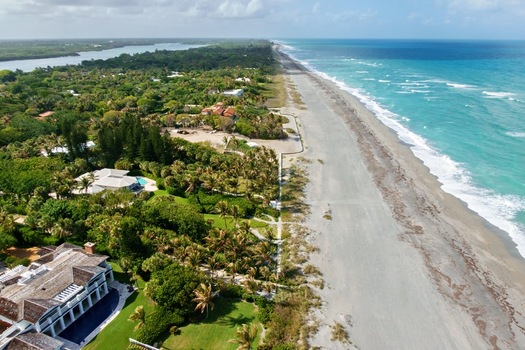 Aerial view of the sandy beach alongside the lush green vegetation and houses with the turquoise ocean waves crashing against the shore Jupiter Island Florida United States. Aerial view of the sandy beach alongside the lush green vegetation and houses with the turquoise ocean waves crashing against the shore Jupiter Island Florida United States.